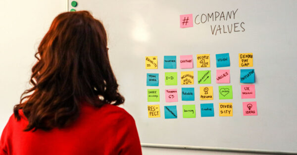 From posters to practice: How to bring your organization's values to life - Photo by Walls.io on Unsplash (A woman standing in front of a white board with company values written on it)